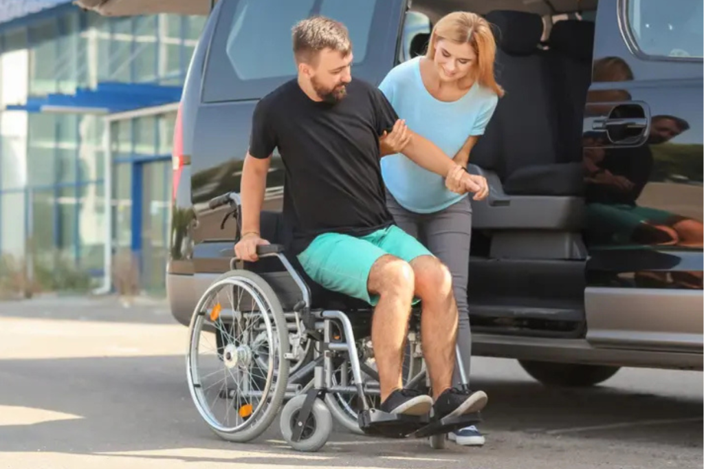 Man being assisted into a wheelchair from a car by his female support worker