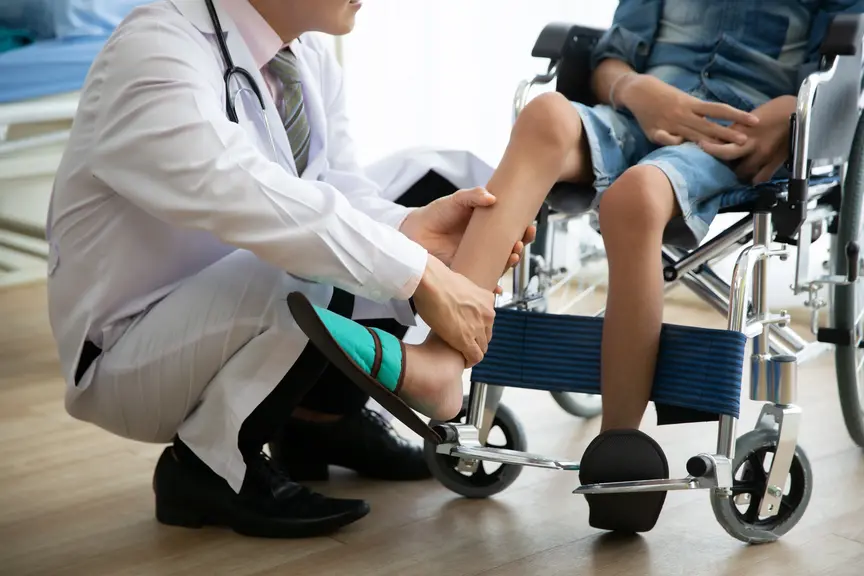 Doctor assessing young boys leg who is in a wheelchair - helping him to recover