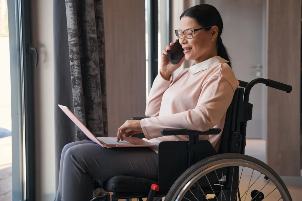 Woman in wheelchair using her laptop and phone to make a referral with Cherry Blossom Care