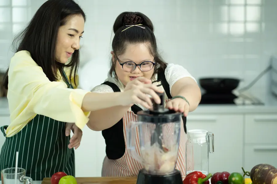 Young woman with Down syndrome and her female support worker making a smoothie
