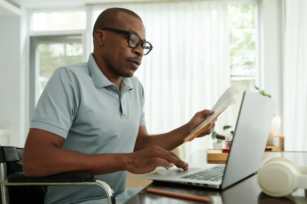 Man in wheelchair sitting at his computer looking through paperwork