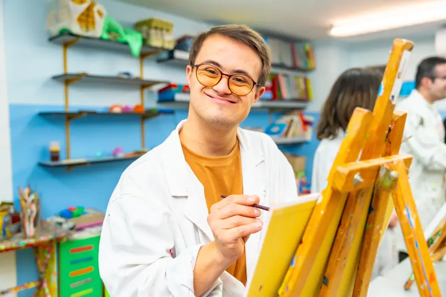 Young man with Down syndrome smiling at the camera while enjoying a group painting class