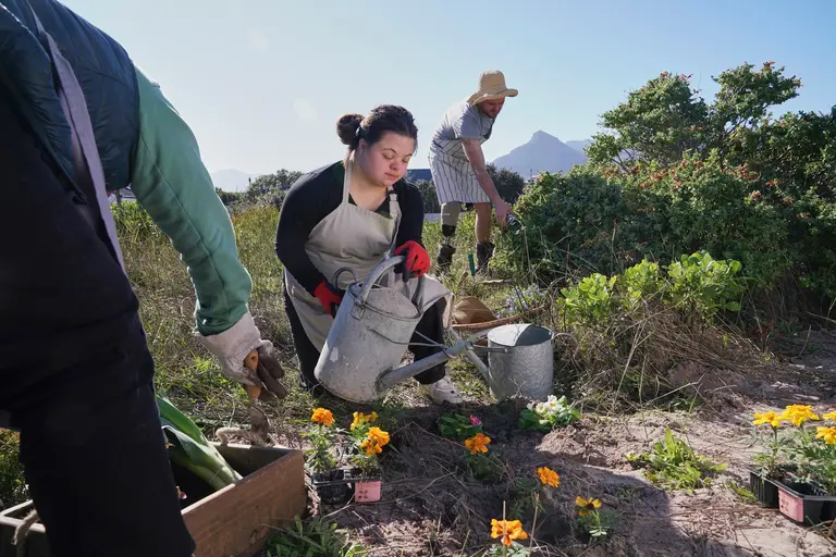Woman with Down syndrome watering a garden with her friends outside